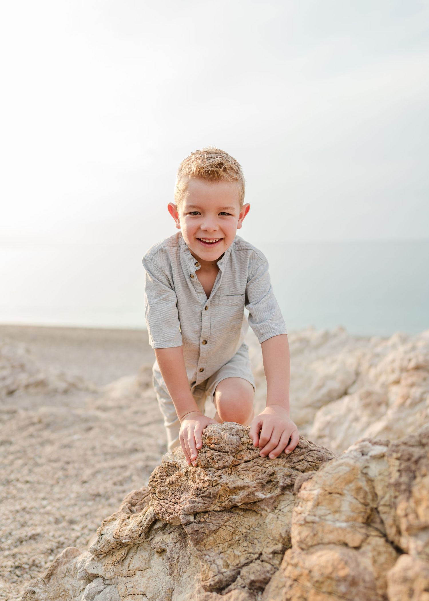 Young child climbing on coastal rocks at beach wearing light colored clothing during sunset. Fotograf Rhodos