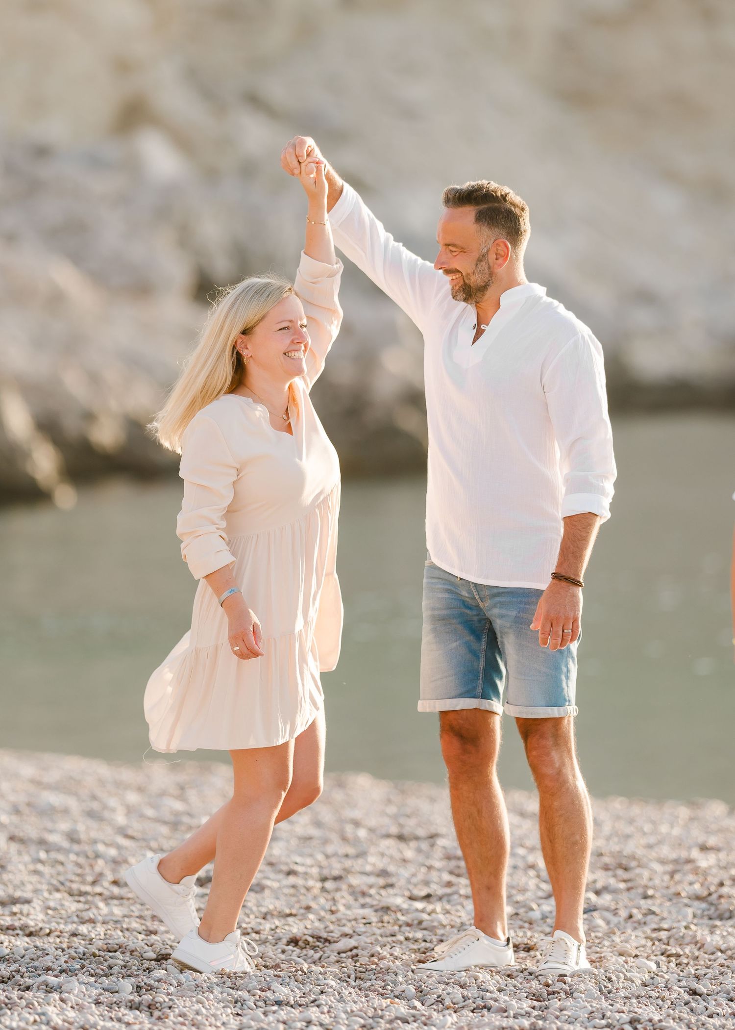 A couple dancing on a pebbly beach with cliffs and water in the background. Fotograf Rhodos