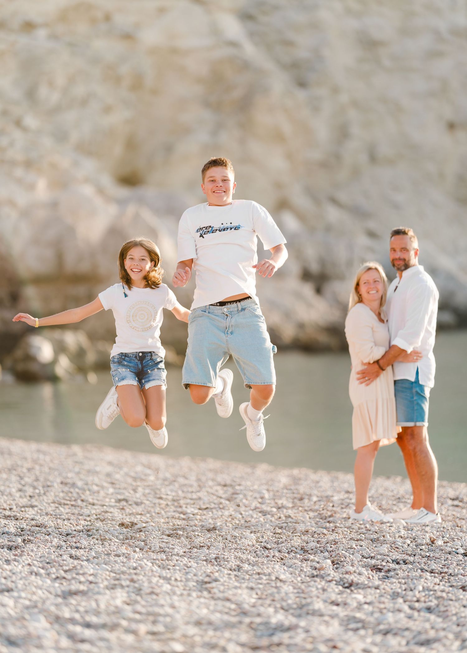 Two people jumping on a rocky beach while others watch in the background. Fotograf Rhodos