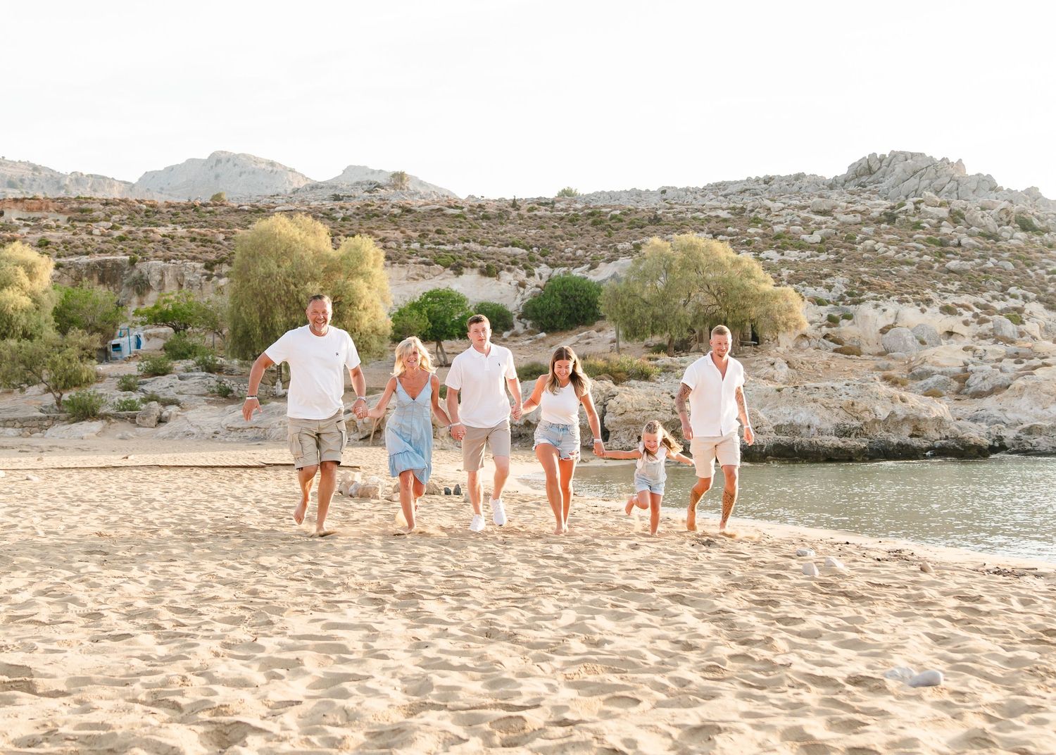 Group walking together on sandy beach with rocky hills in background during sunset. Fotograf Rhodos