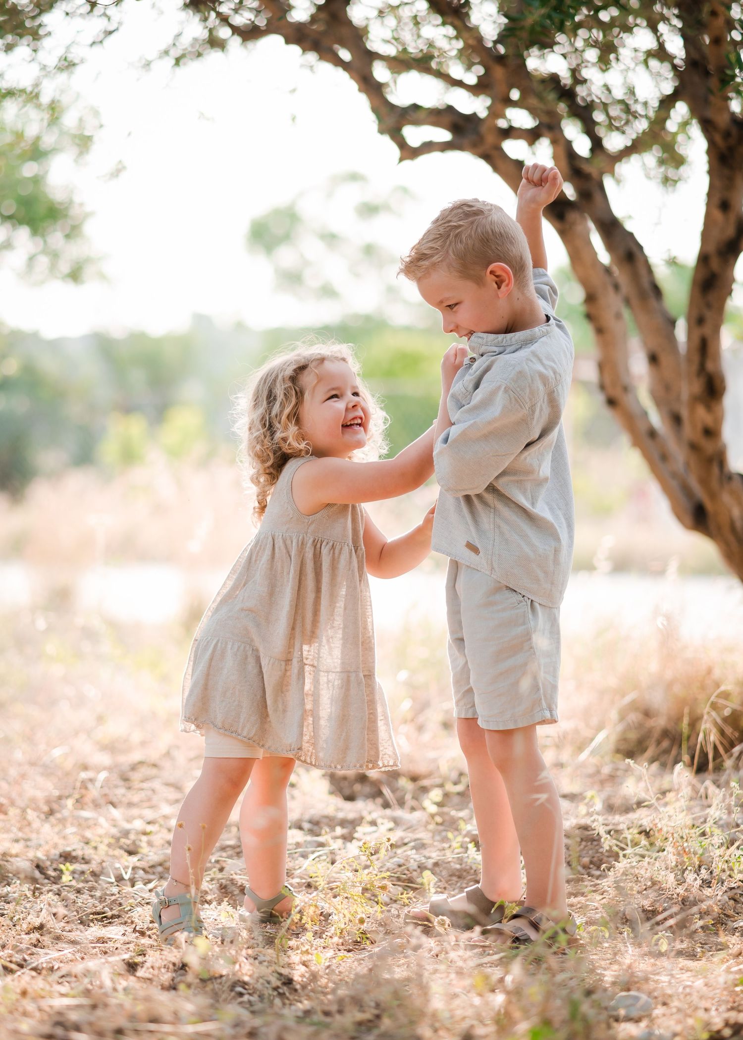 Playful interaction between two young children on a sunlit grassy field under trees. Fotograf Rhodos