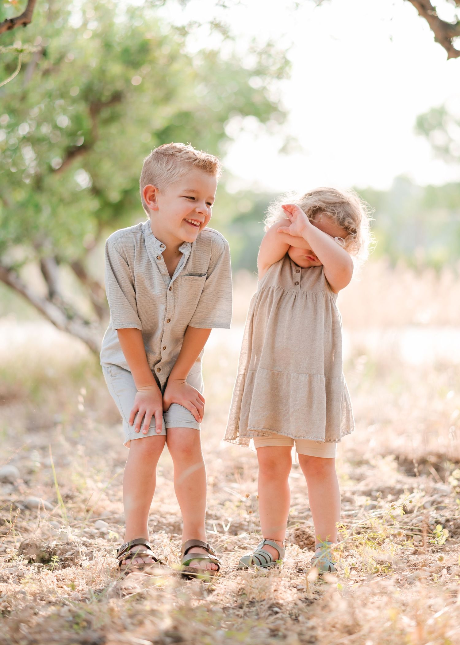 Two children share a laugh together on a sunny day under trees. Fotograf Rhodos