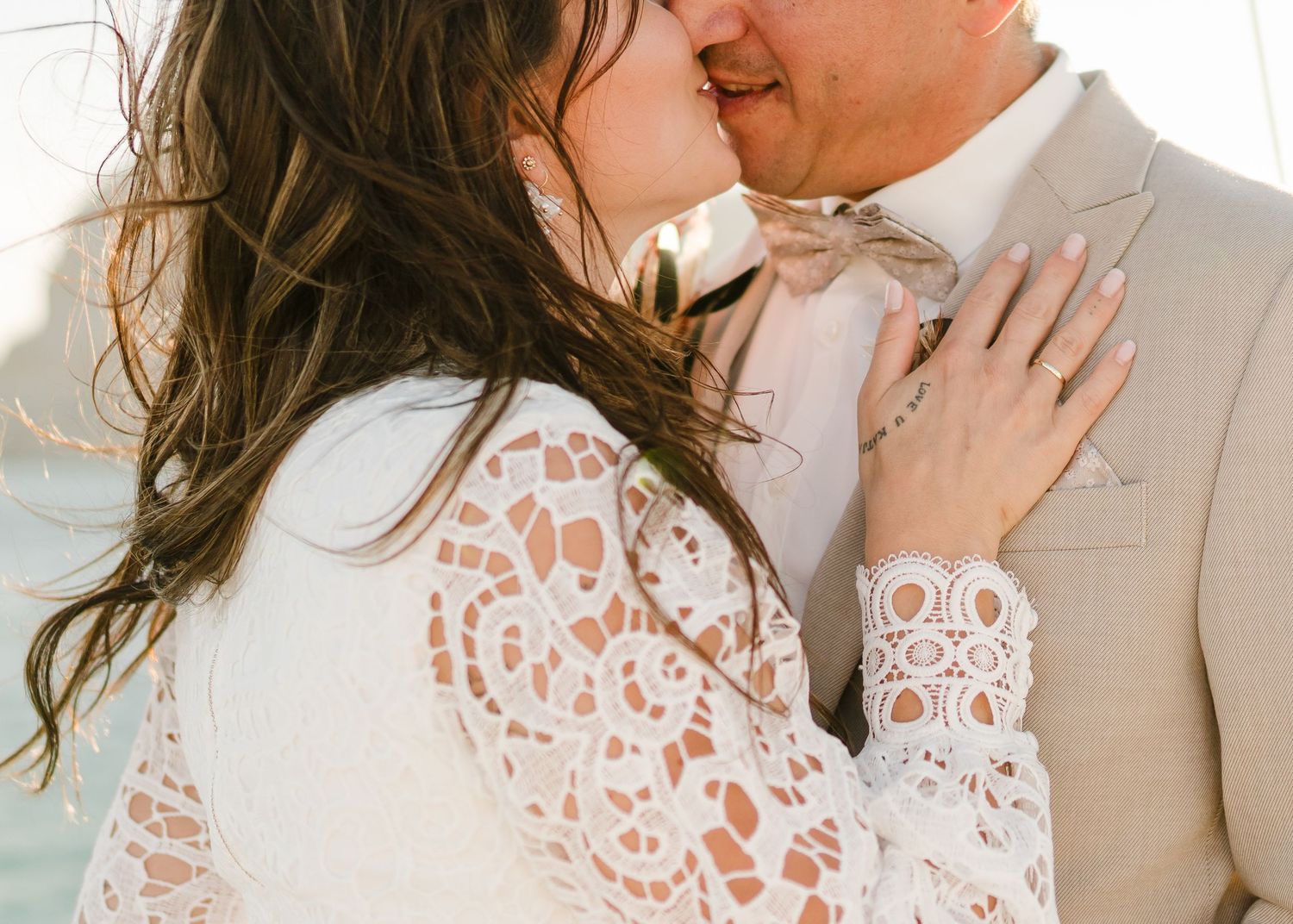 Nahaufnahme einer romantischen Umarmung mit Spitzenärmeldetails und einem beigen Anzug bei einer Hochzeit am Meer. heiraten am Strand - Hoch