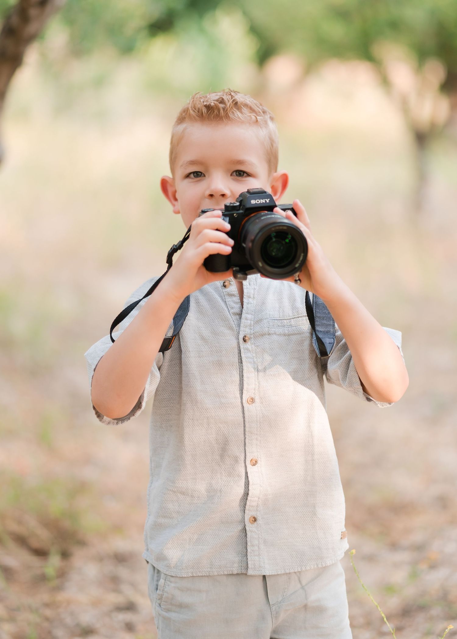 A young child holds a professional camera while taking pictures outdoors. Fotograf Rhodos