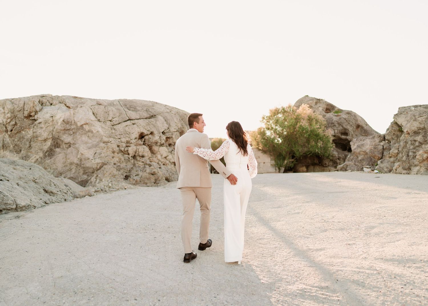Paar hält sich an den Händen und geht während des Fotoshootings zur Hochzeit bei Sonnenuntergang gemeinsam in der Wüstenlandschaft spazieren
