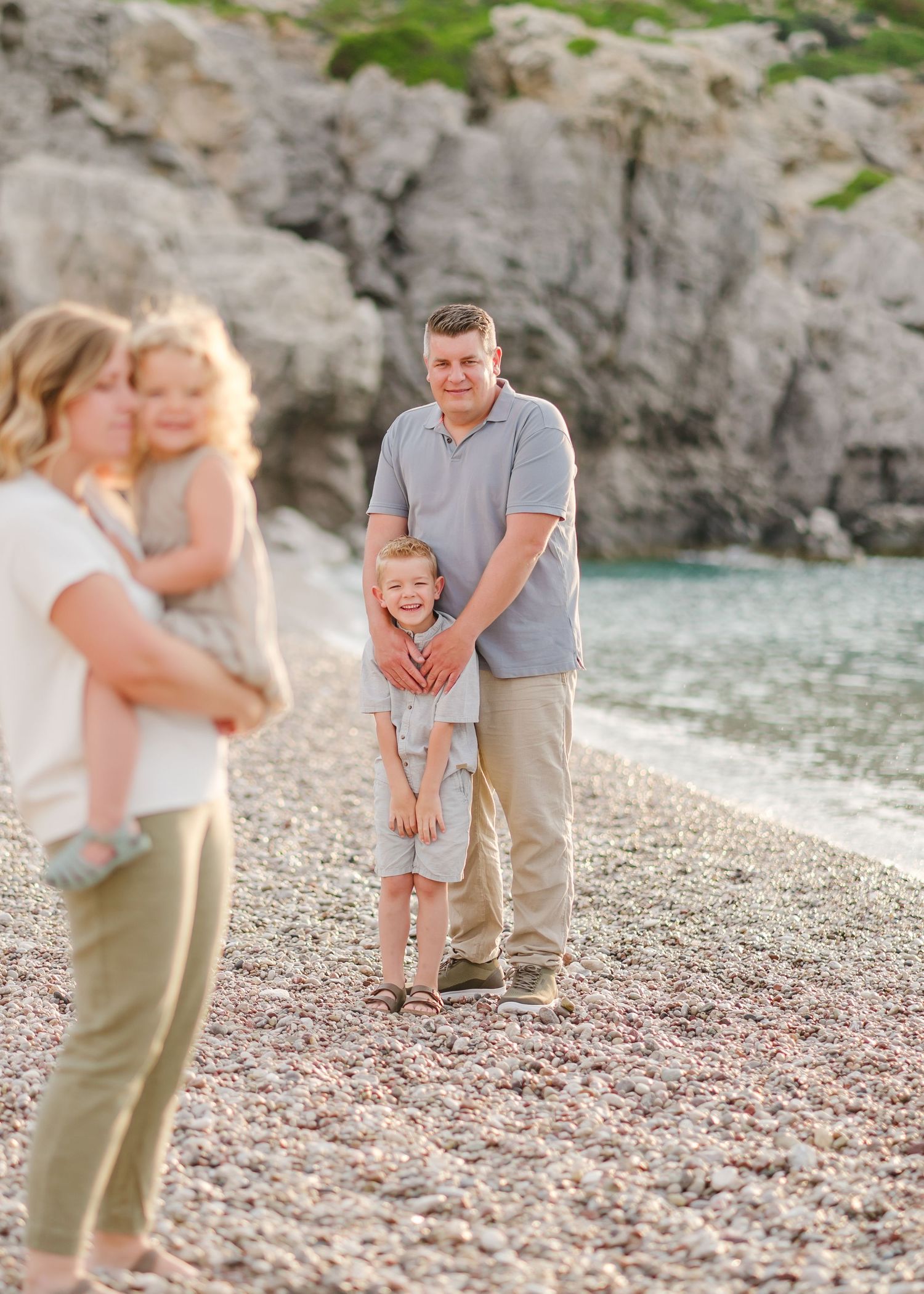 Candid family beach portrait with rocky coastline and turquoise water in background. Fotograf Rhodos