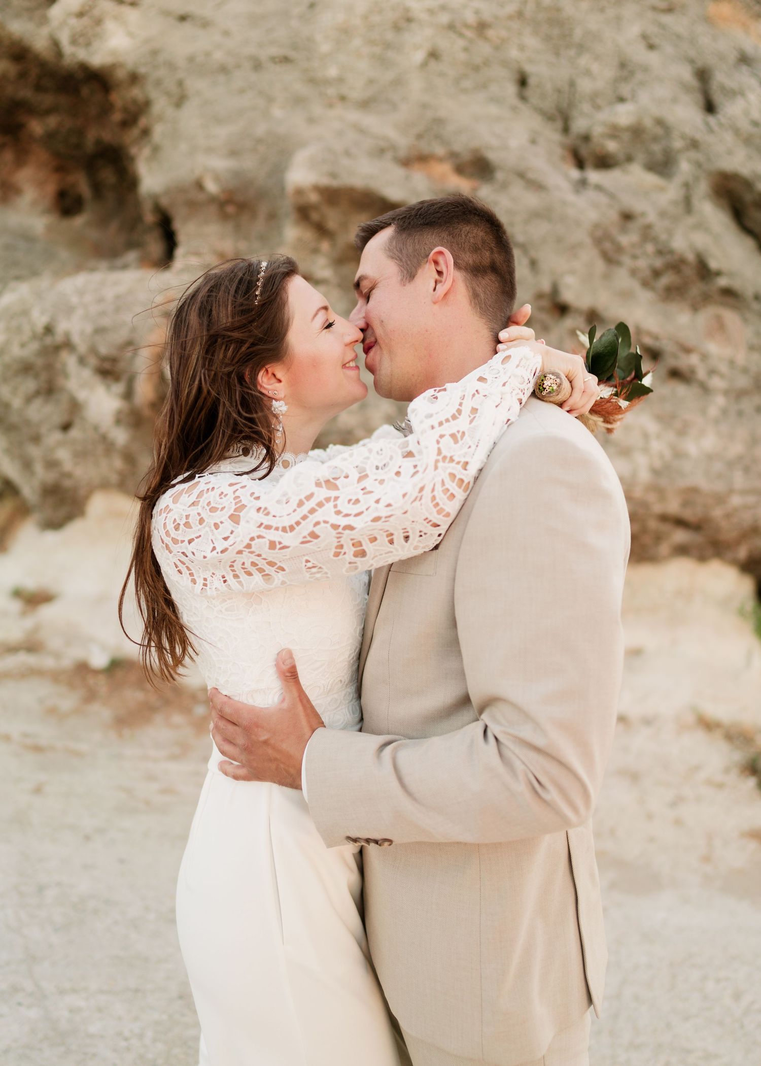 Zärtliche Umarmung zwischen Frischvermählten in Wüstenlandschaft mit natürlichen Felsformationen. heiraten am Strand - Hochzeitsfotograf Rho