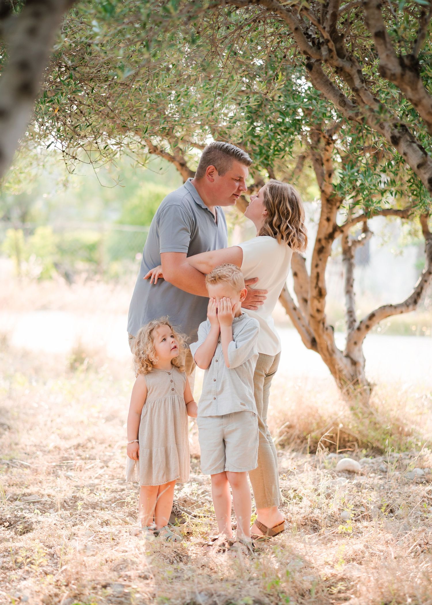 A sweet family moment captured under olive trees in warm sunlight. Fotograf Rhodos