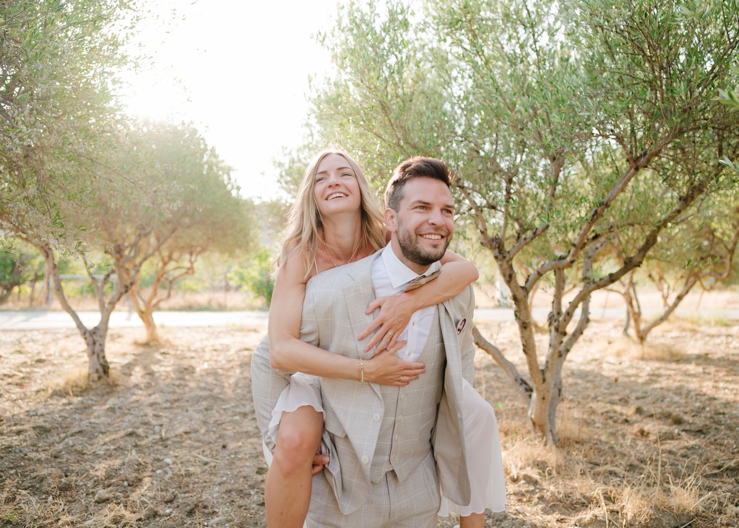 Sorgloses Paar in Hochzeitskleidung, das einen verspielten Moment in rustikaler Outdoor-Umgebung teilt. Fotografin Rhodos - Hochzeitsfotogra