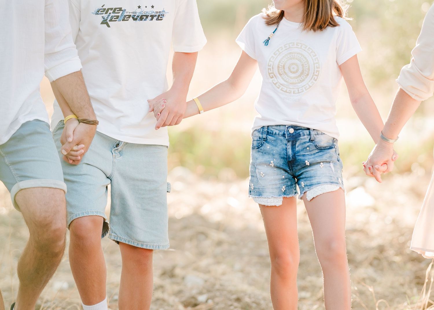 Close-up view of coordinated summer outfits with white shirts and blue shorts while holding hands. Fotograf Rhodos
