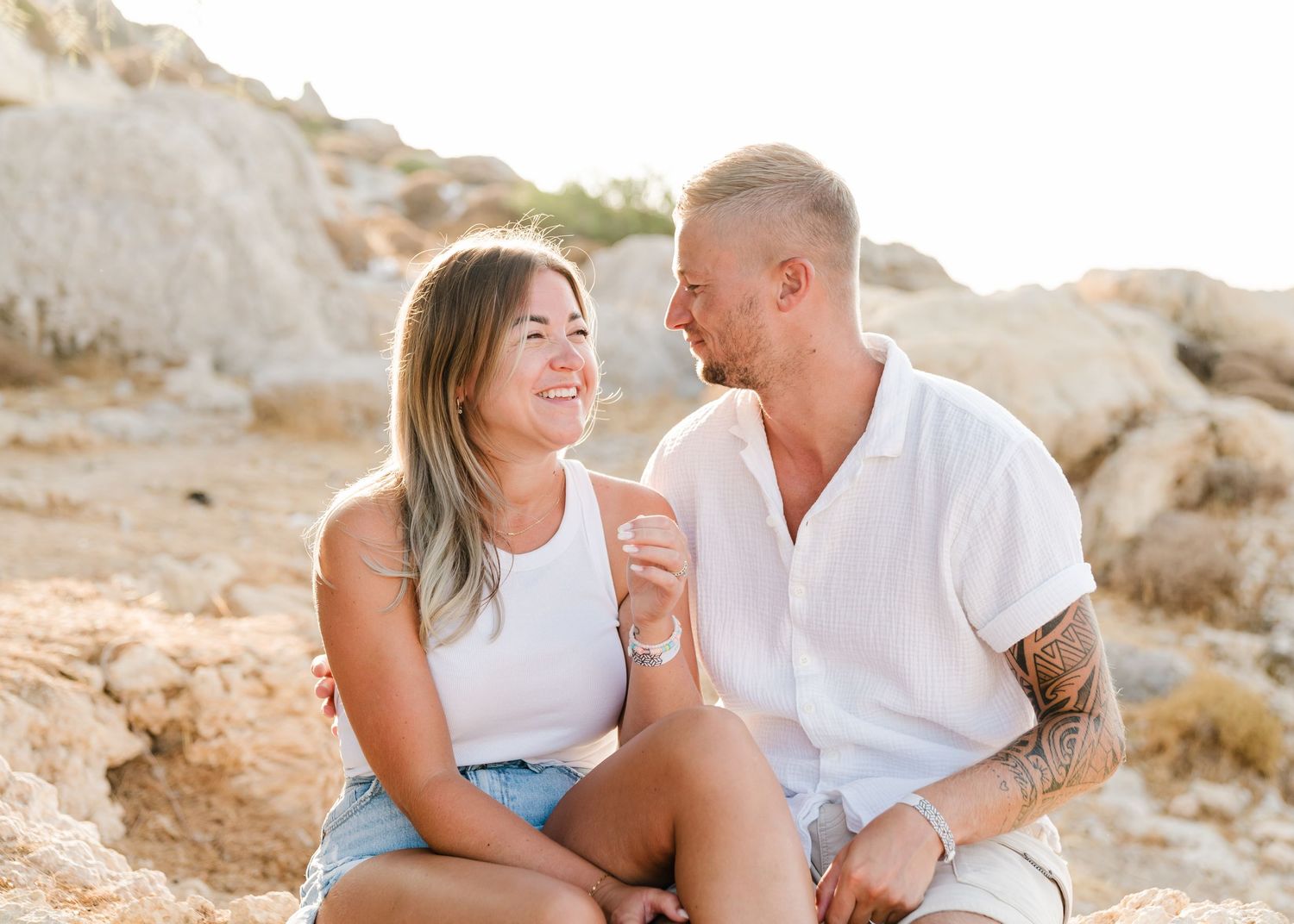 Happy couple sharing candid moment while sitting on rocky terrain at sunset. Fotograf Rhodos