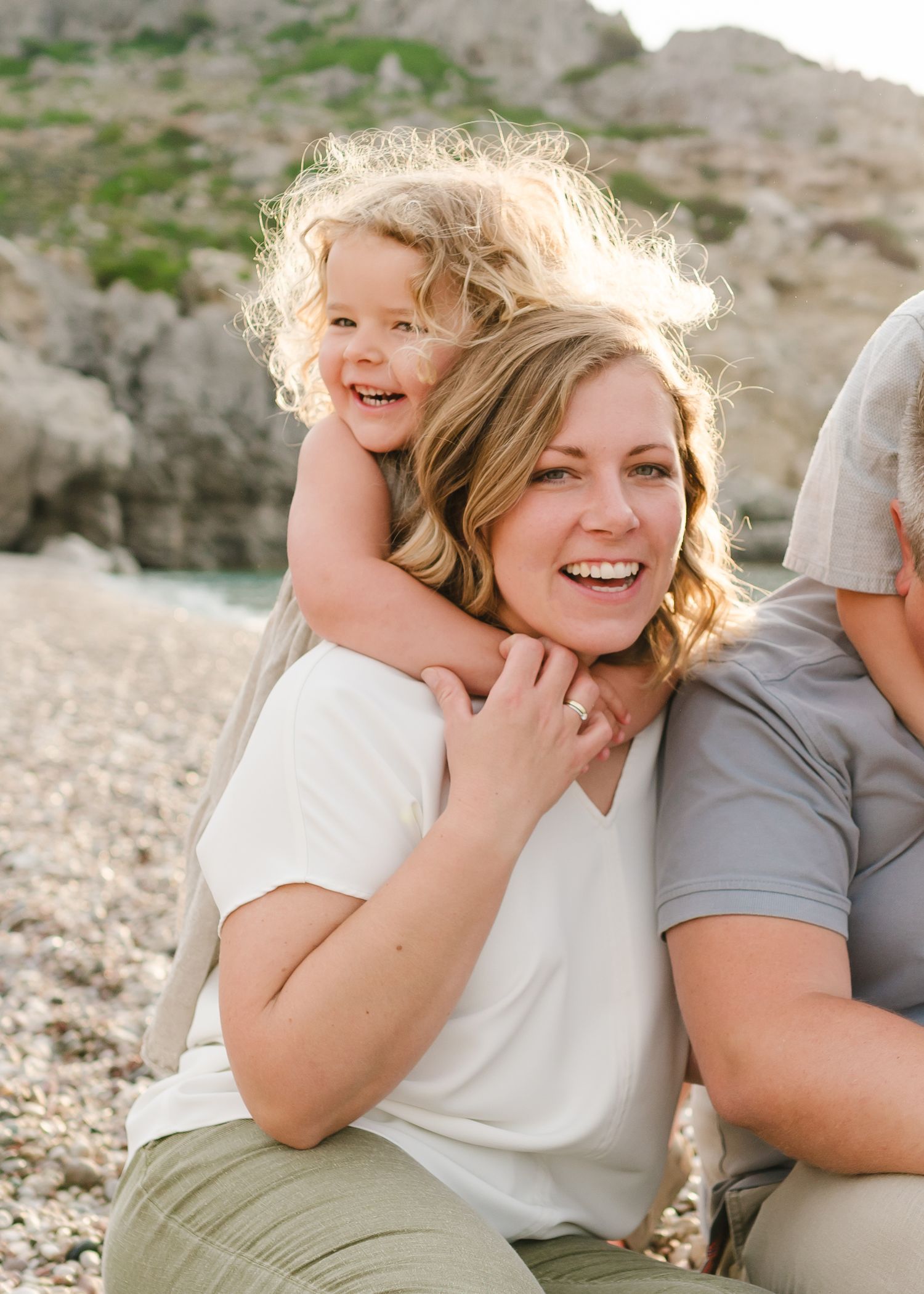 Family members share a playful piggyback moment on a rocky beach. Fotograf Rhodos
