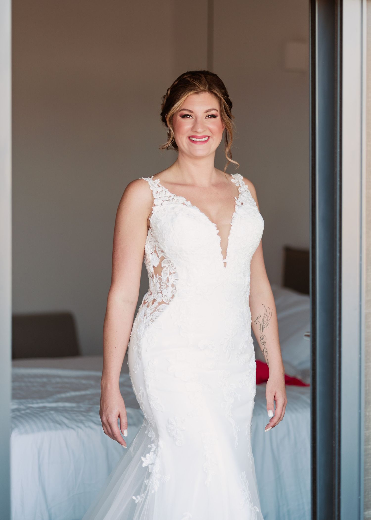 A bride poses in a fitted white lace wedding gown with plunging neckline in a hotel room settiFotograf Trauung Rhodos - Hochzeitsfotografng.