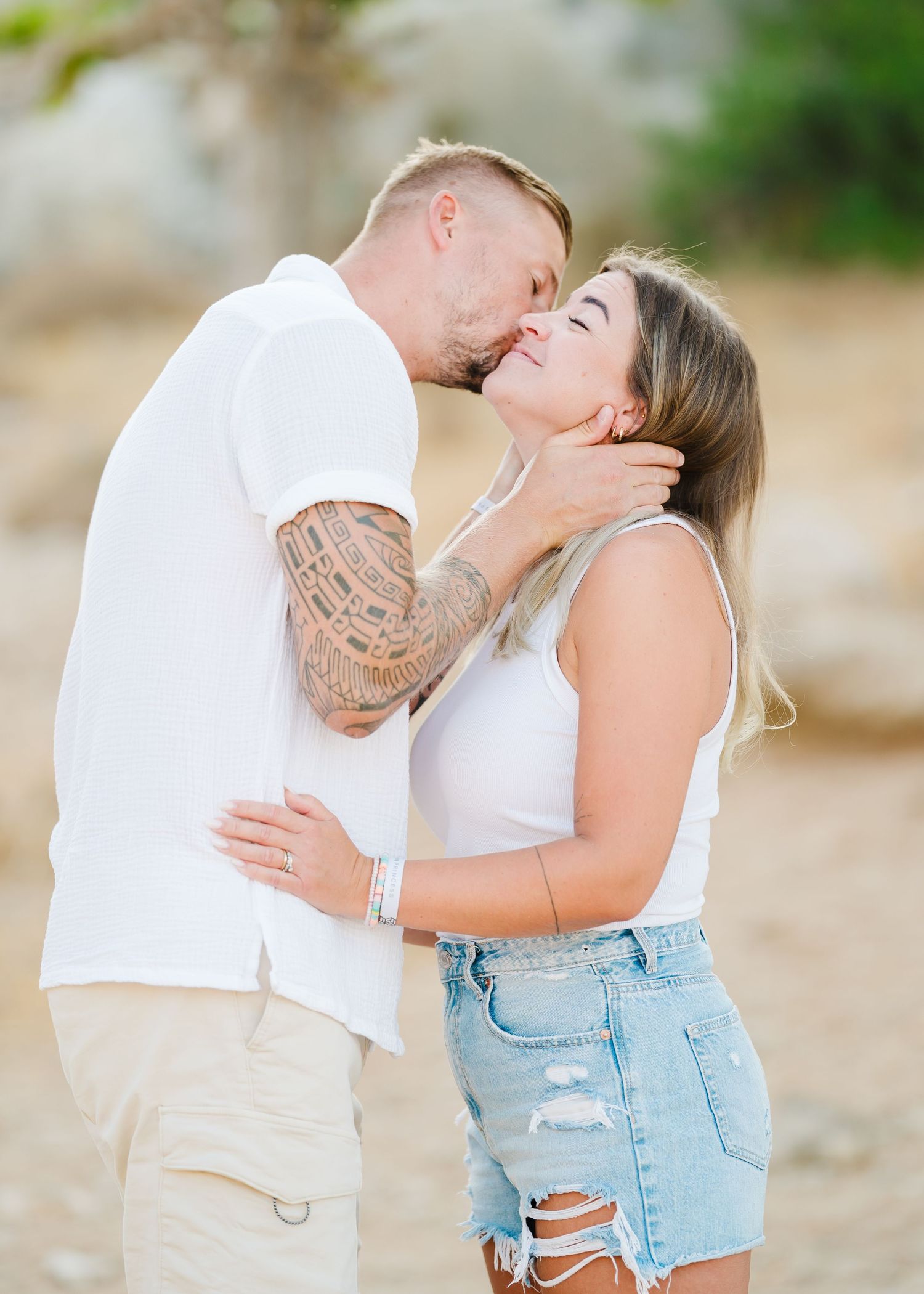 Couple sharing an intimate moment outdoors wearing coordinated white outfits against a natural rocky backdrop. Fotograf Rhodos