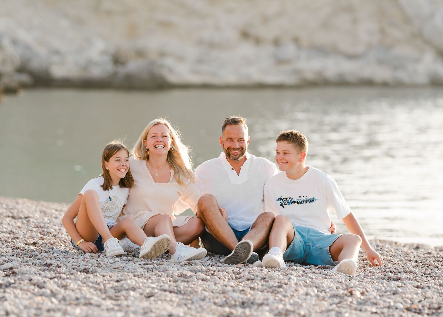 A casual group photo on a beach with rocky cliffs and water in the background. Fotograf Rhodos