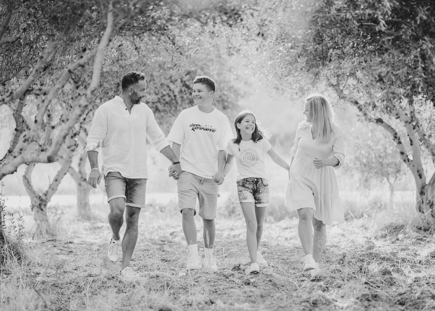 Black and white photo of a group walking through an olive grove while holding hands. Fotograf Rhodos