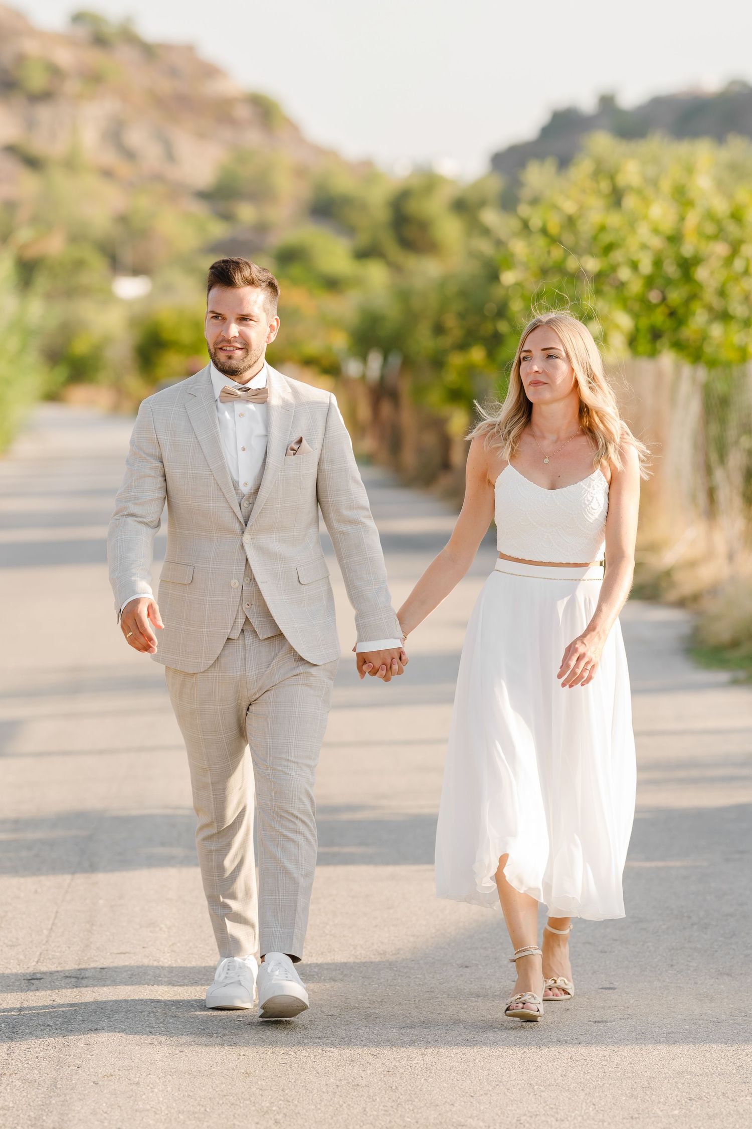 Elegantes Paar in heller Hochzeitskleidung, das Hand in Hand auf dem Landweg schlendert. Fotografin Rhodos - Hochzeitsfotograf Rhodos Tina L