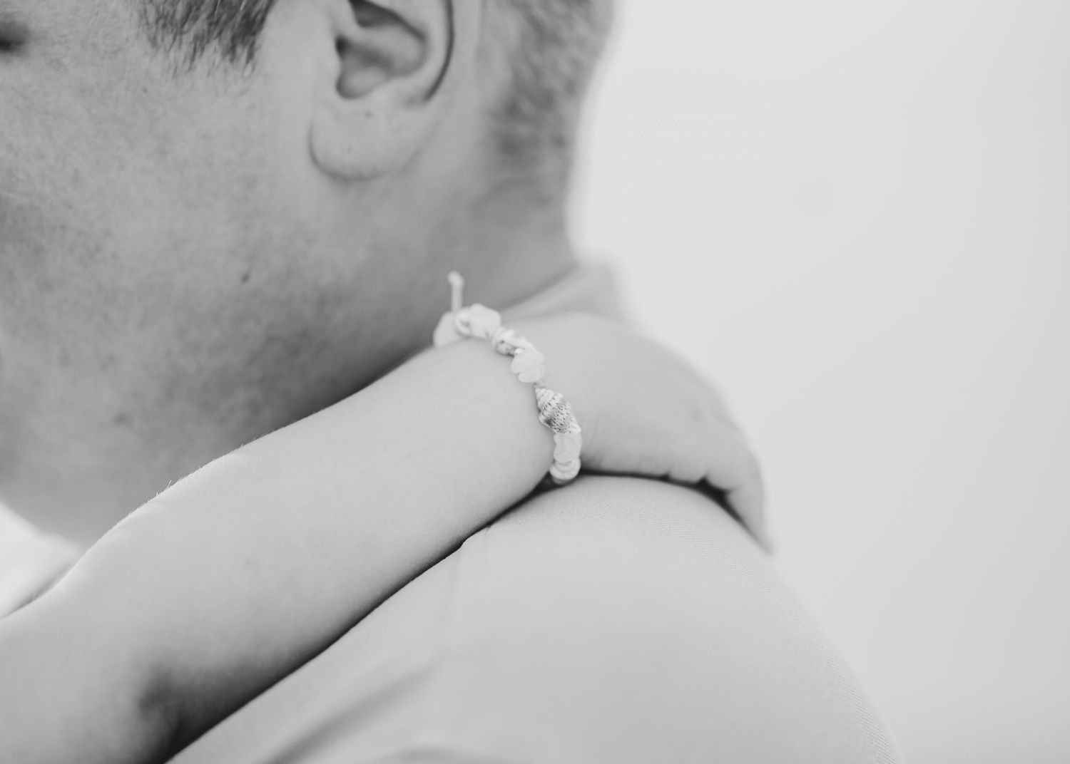 Black and white close-up showing a delicate bracelet on an arm during an embrace. Fotograf Rhodos