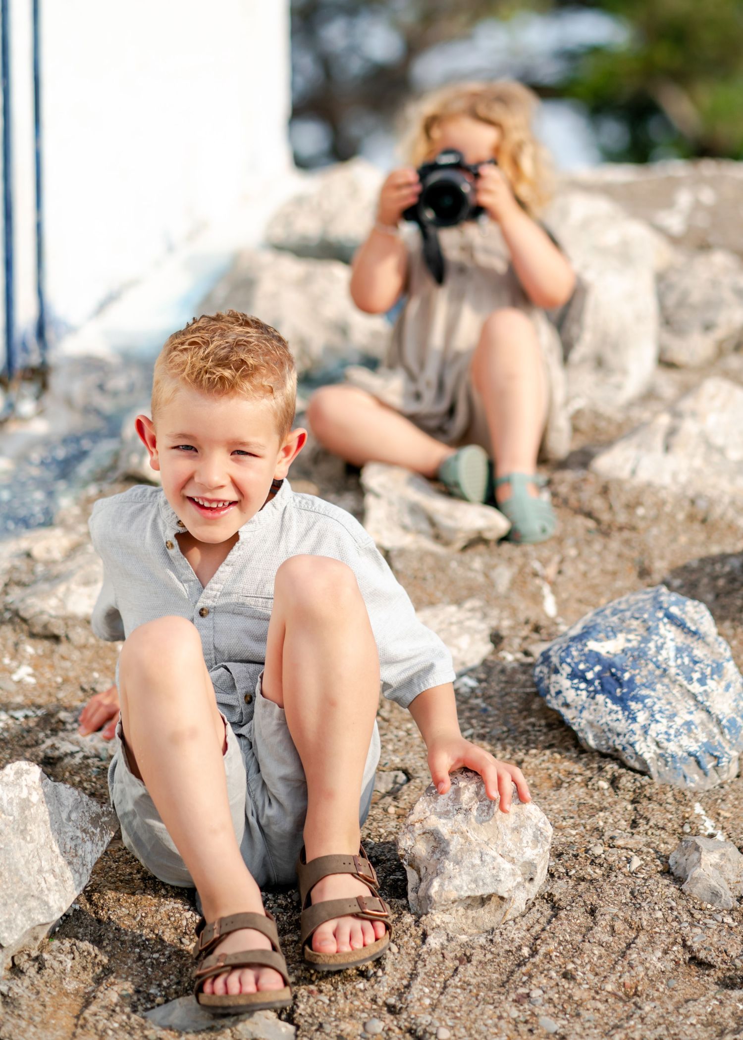 Young child plays on rocky beach terrain wearing sandals during summer photo session. Fotograf Rhodos