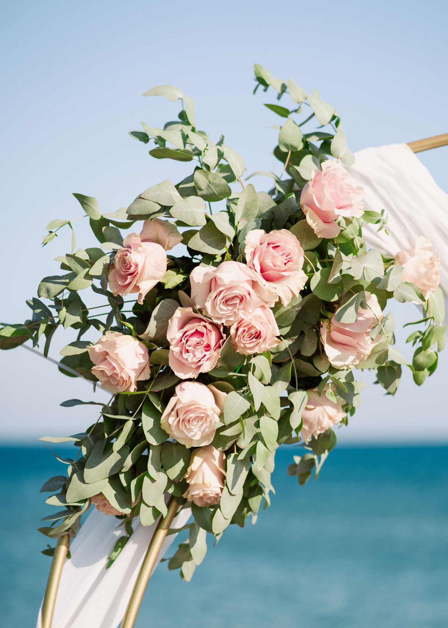 Lush bouquet of pink roses and eucalyptus leaves against turquoise ocean background.