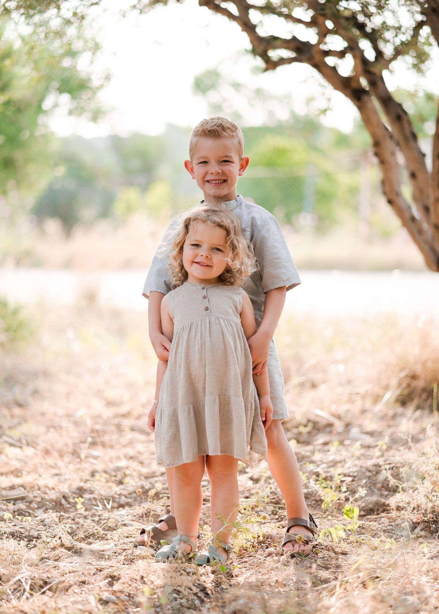 Two children pose together in coordinating outfits under a tree. Fotograf Rhodos