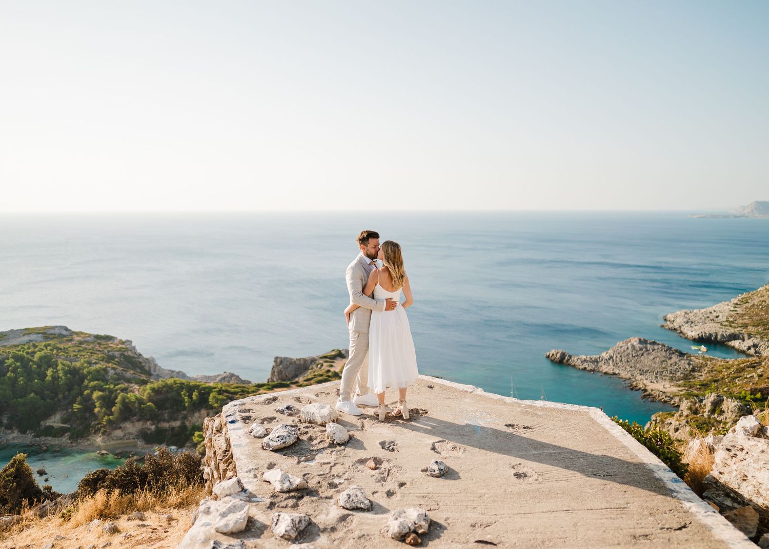 Das Paar steht auf einer Aussichtsplattform an der Küste mit Blick auf das blaue Mittelmeer und felsige Buchten. Strandhochzeit Rhodos - Hoc