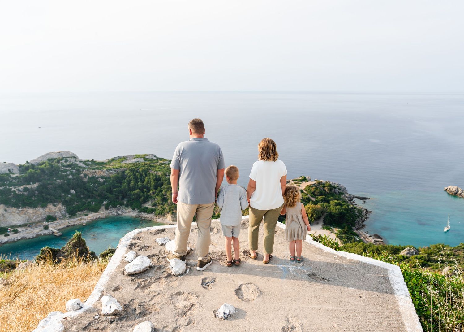 Family sitting together overlooking a scenic coastal vista from a clifftop viewpoint. Fotograf Rhodos