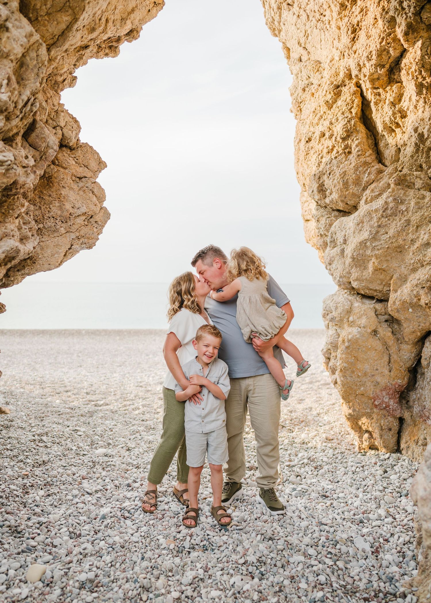 Family sharing an affectionate moment framed by rocky arch at seaside. Fotograf Rhodos