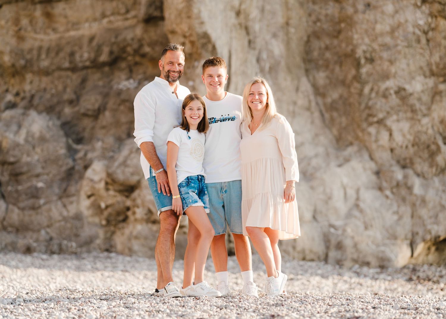A group poses casually on a rocky Mediterranean beach with limestone cliffs behind them. Fotograf Rhodos