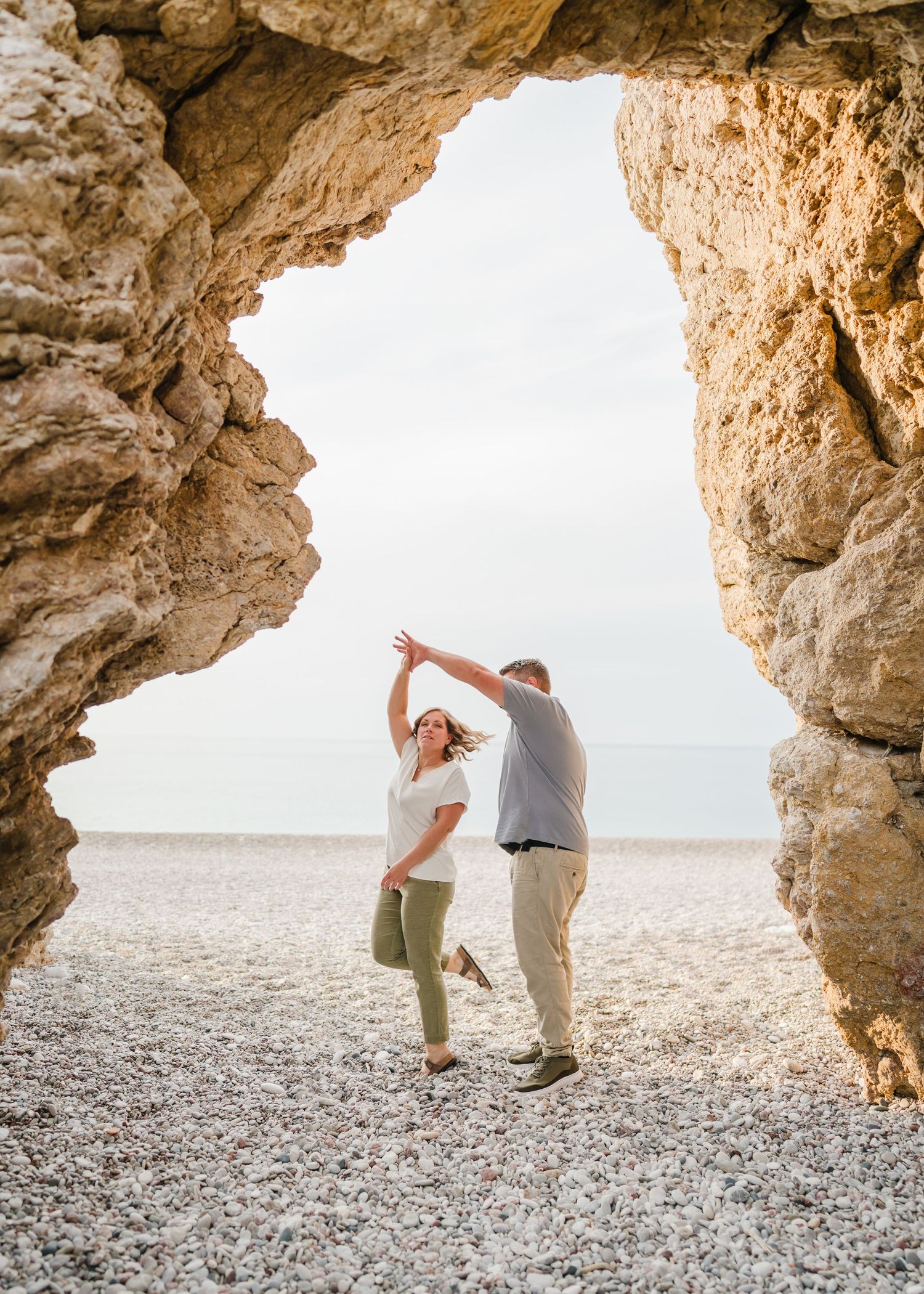 Couple dancing together under natural stone arch at beach during golden hour. Fotograf Rhodos