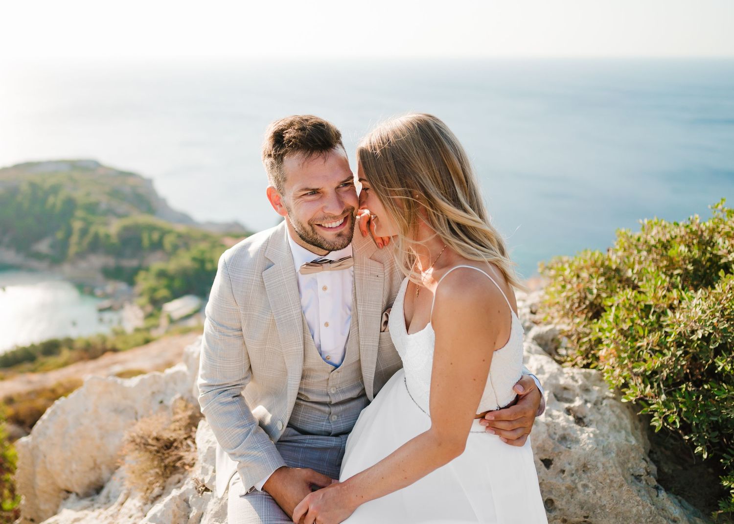 Glückliches Paar lacht zusammen, während es auf Küstenfelsen mit Meerblick sitzt. Fotografin Rhodos - Hochzeitsfotograf Rhodos Tina Lucius