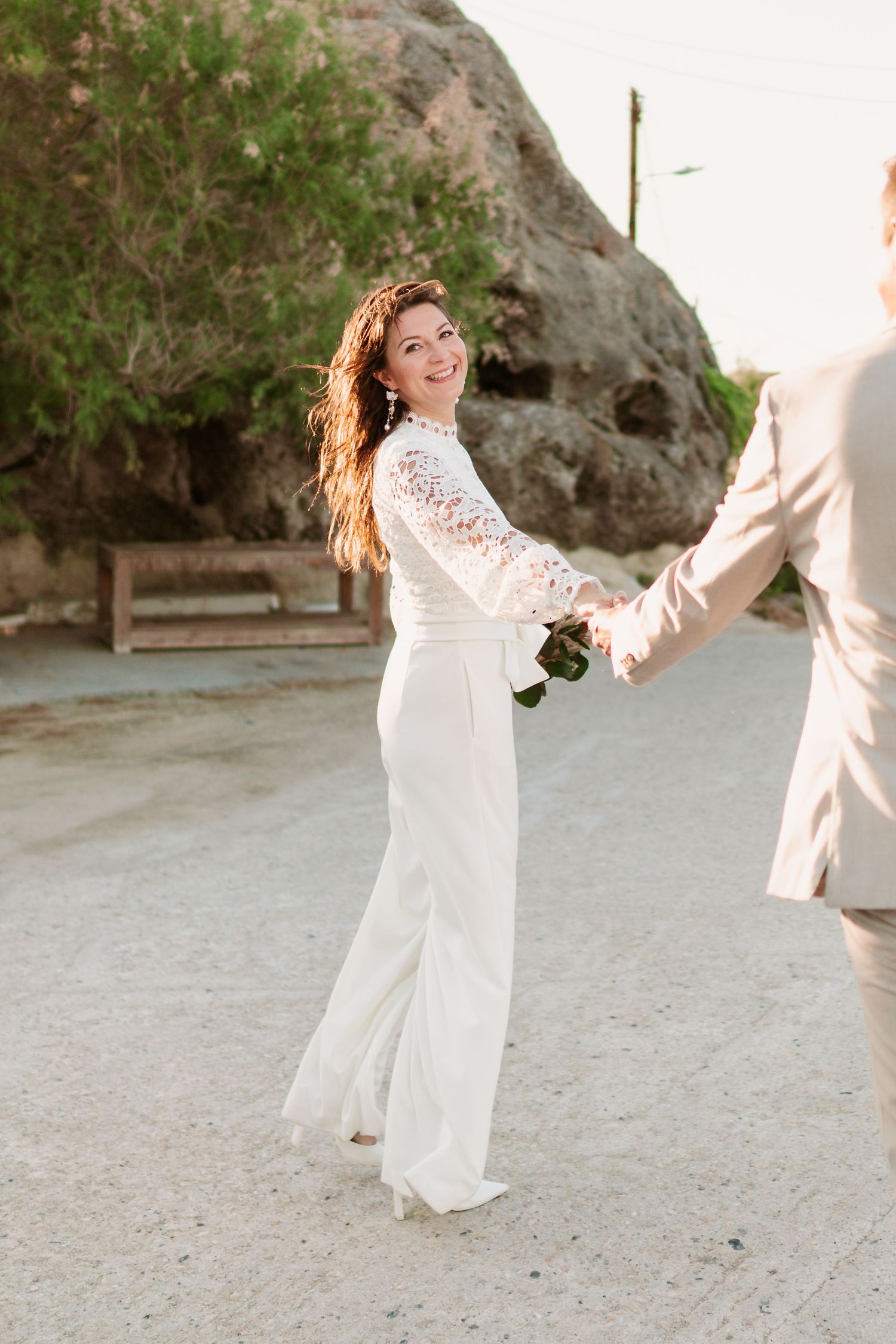 Paar tanzt während des Fotoshootings bei Sonnenuntergang freudig in weißen Outfits gegen Wüstenfelsen. Strandhochzeit Rhodos - Hochzeitsfoto