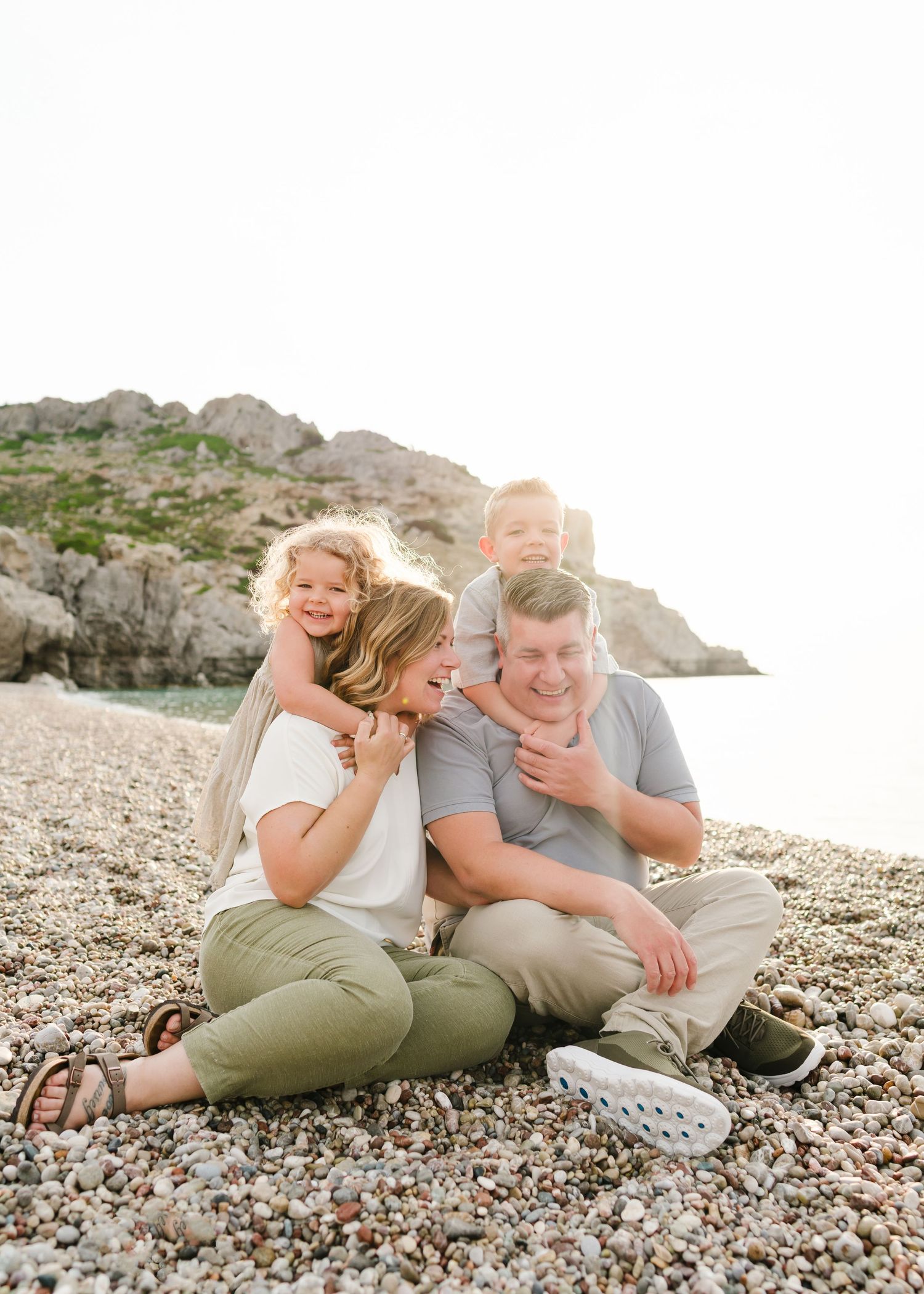 Family shares laughs while sitting together on rocky beach near cliffs. Fotograf Rhodos