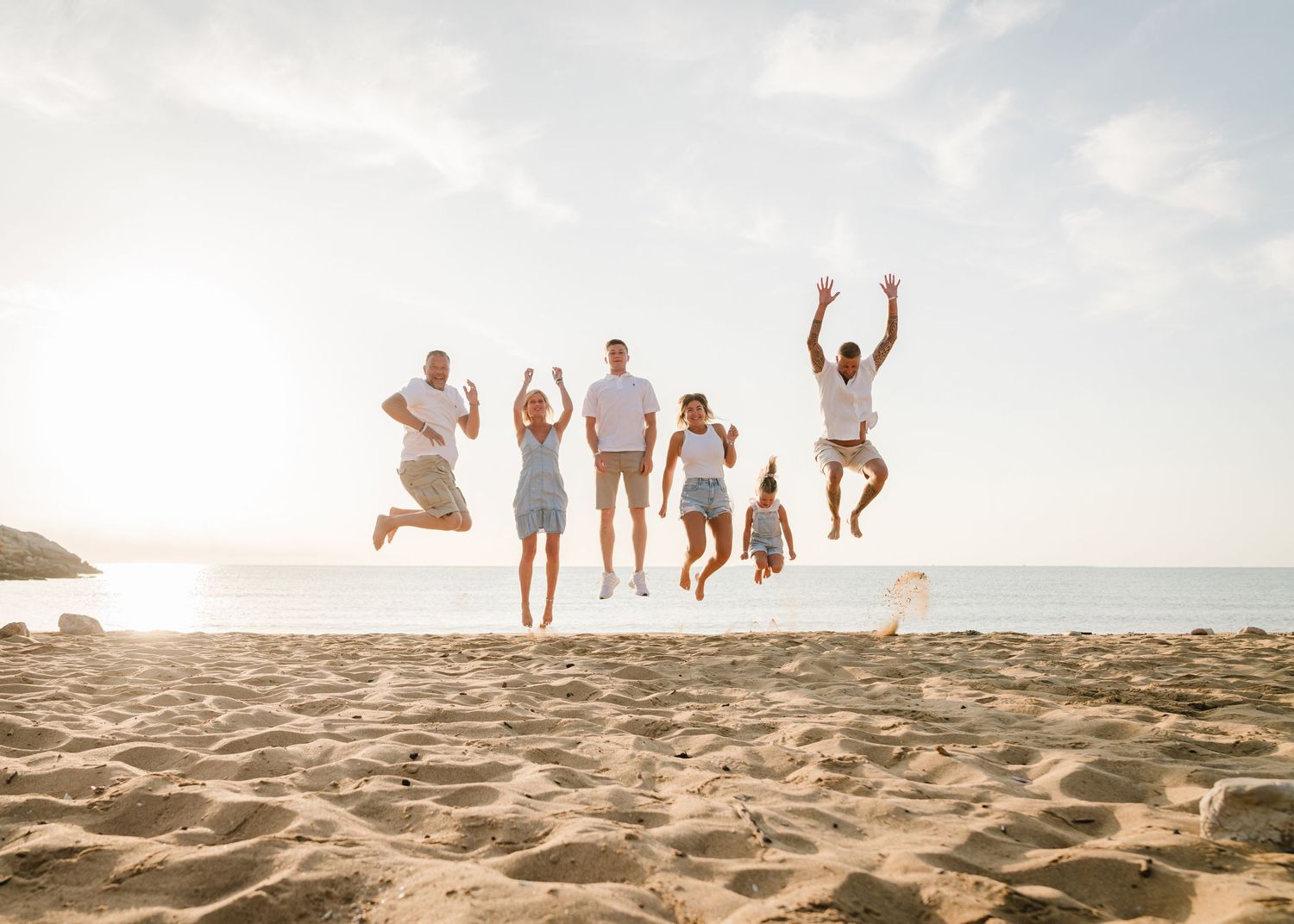 Group of people jumping in unison on beach with ocean and cliffs in background. Fotograf Rhodos