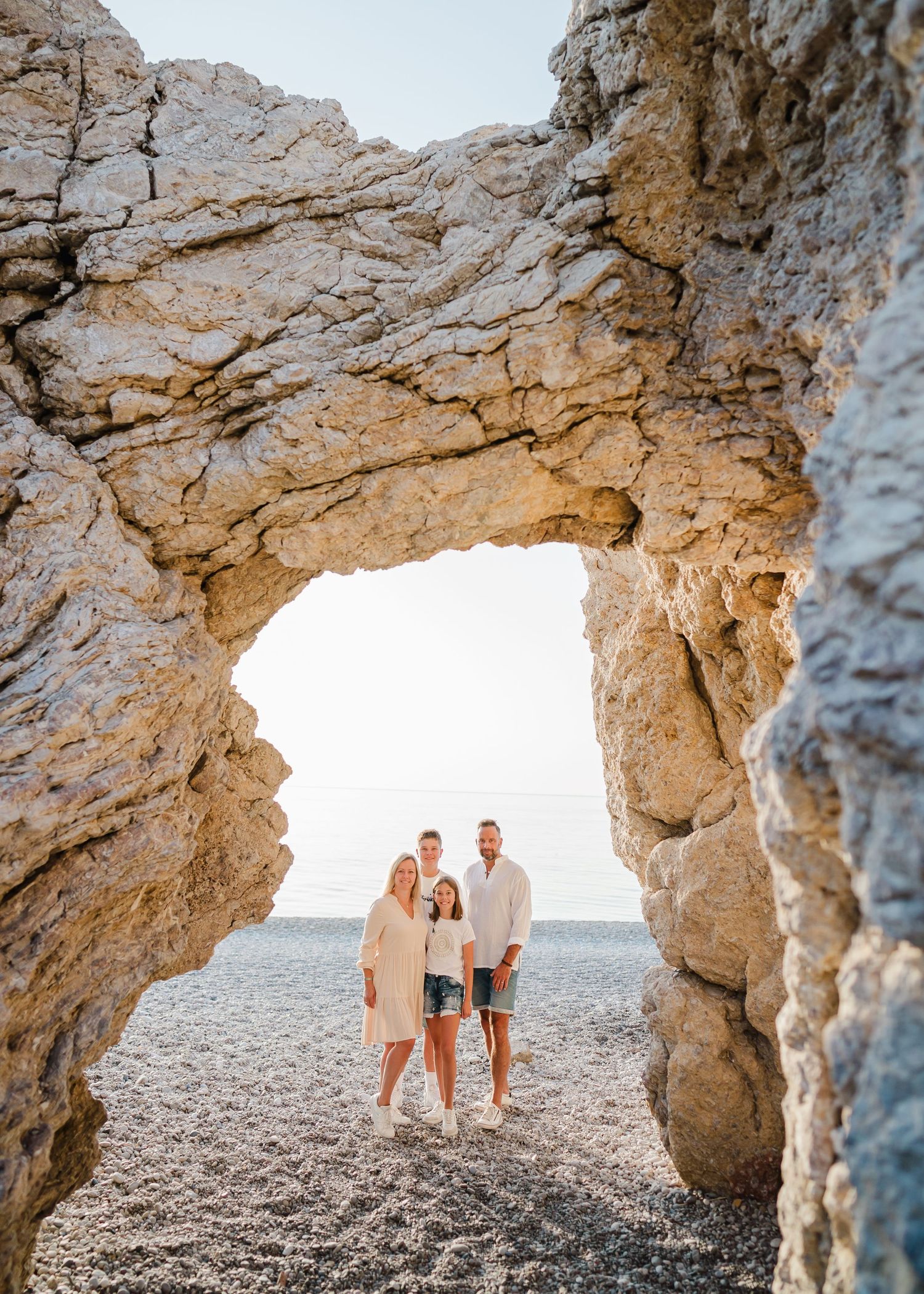 Family silhouetted through natural stone arch formation at sunset on rocky beach. Fotograf Rhodos