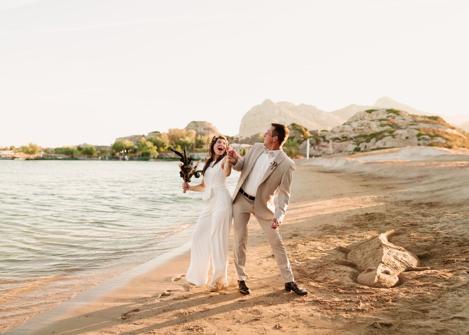 Freudiges Hochzeitspaar tanzt an einem mediterranen Strand mit Klippen im Hintergrund. heiraten am Strand - Hochzeitsfotograf Rhodos Tina Lu