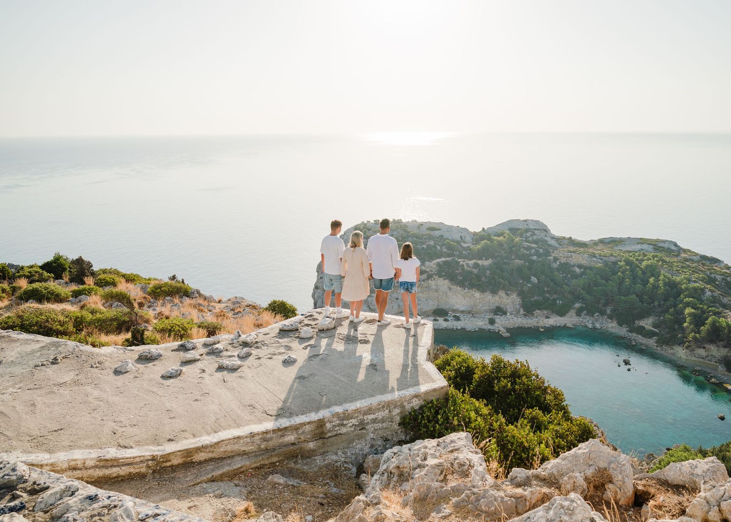Two people sitting on a cliff edge overlooking a beautiful Mediterranean bay with turquoise waters. Fotograf Rhodos