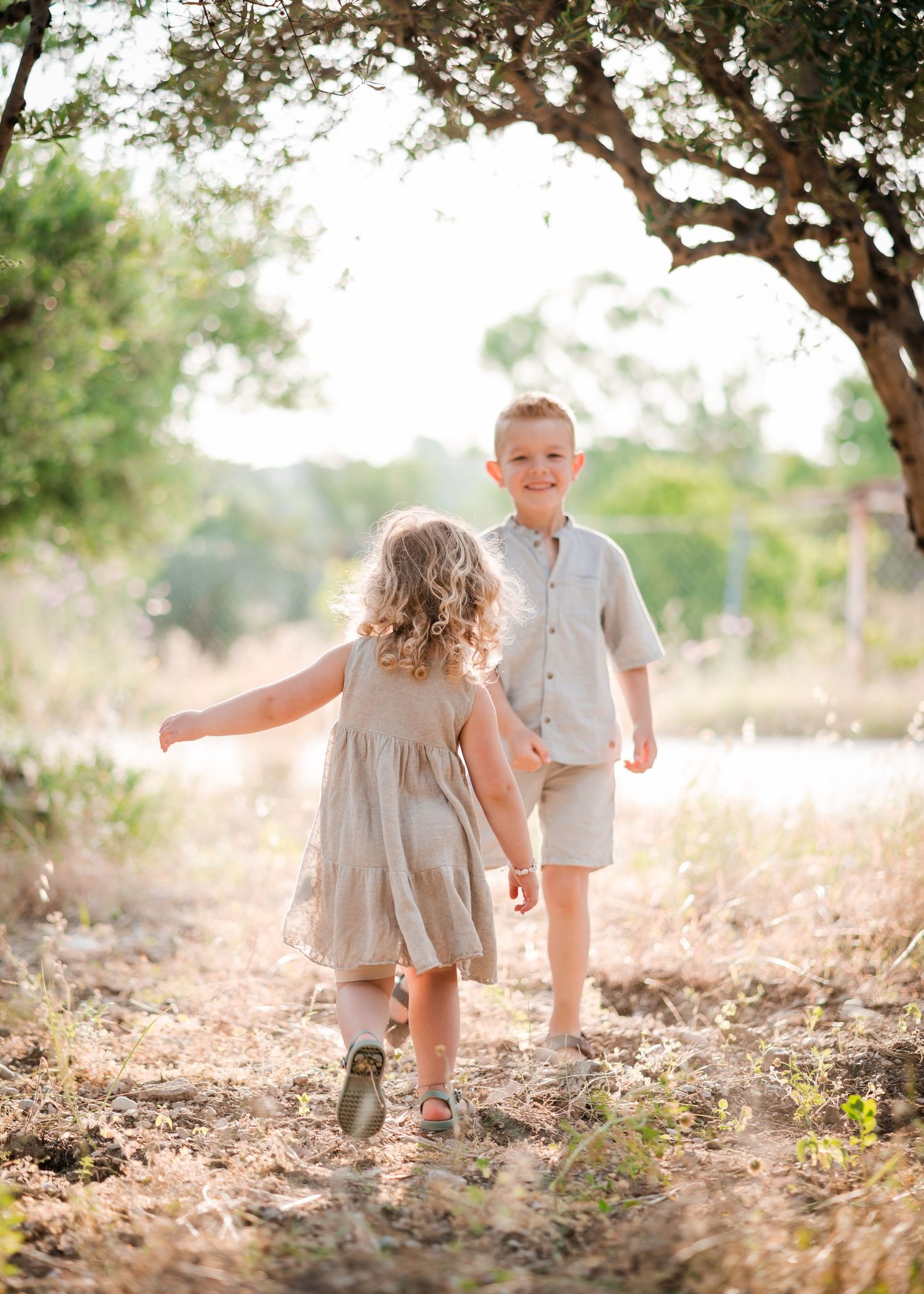 Two children playing together in a sunny outdoor setting wearing light neutral clothing. Fotograf Rhodos