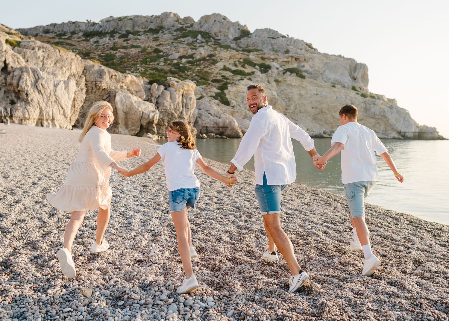 Back view of family holding hands while walking on pebble beach near coastal cliffs. Fotograf Rhodos
