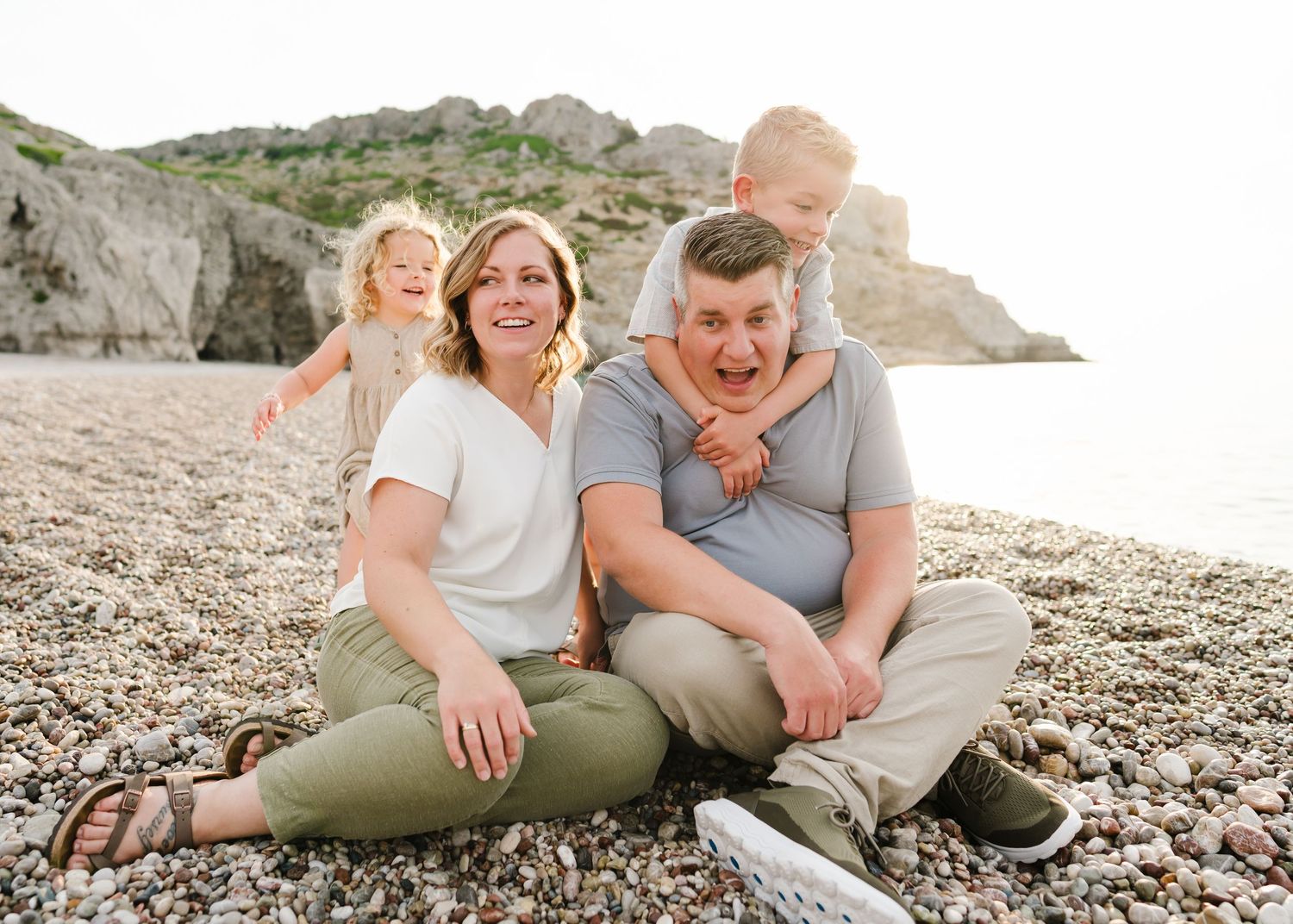 Family sits together on pebble beach with rocky cliffs in background. Fotograf Rhodos
