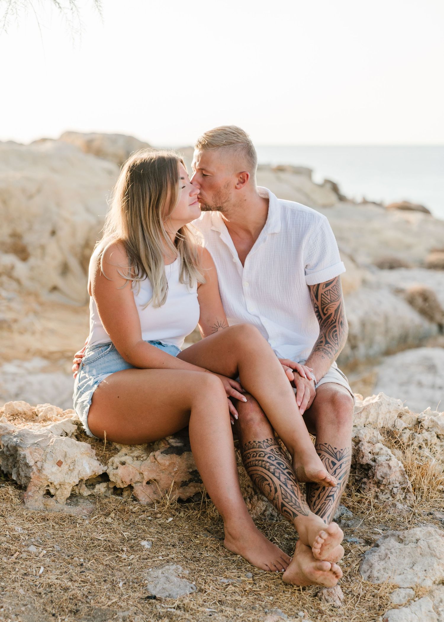 Couple sitting together on rocky coastal outcrop during golden hour. Fotograf Rhodos