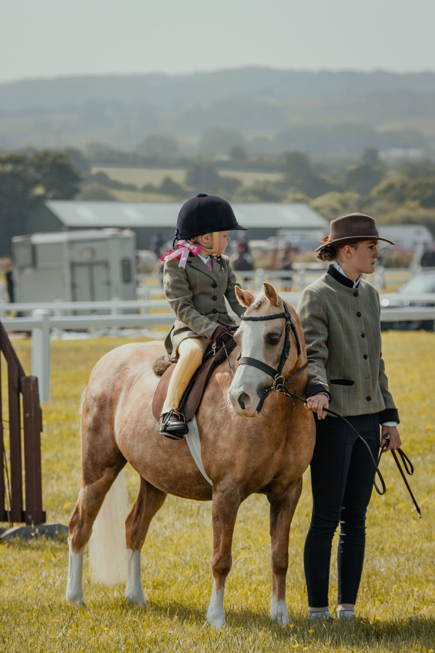 A palomino pony and handlers at an equestrian show in a countryside setting.