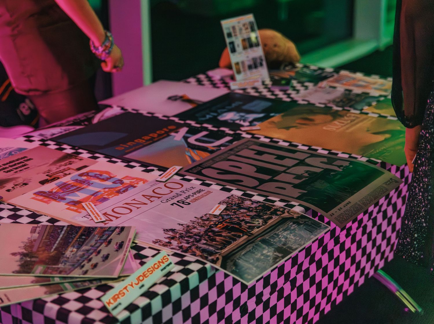 Colorful display of photographs and prints laid out on a checkered surface under pink lighting.
