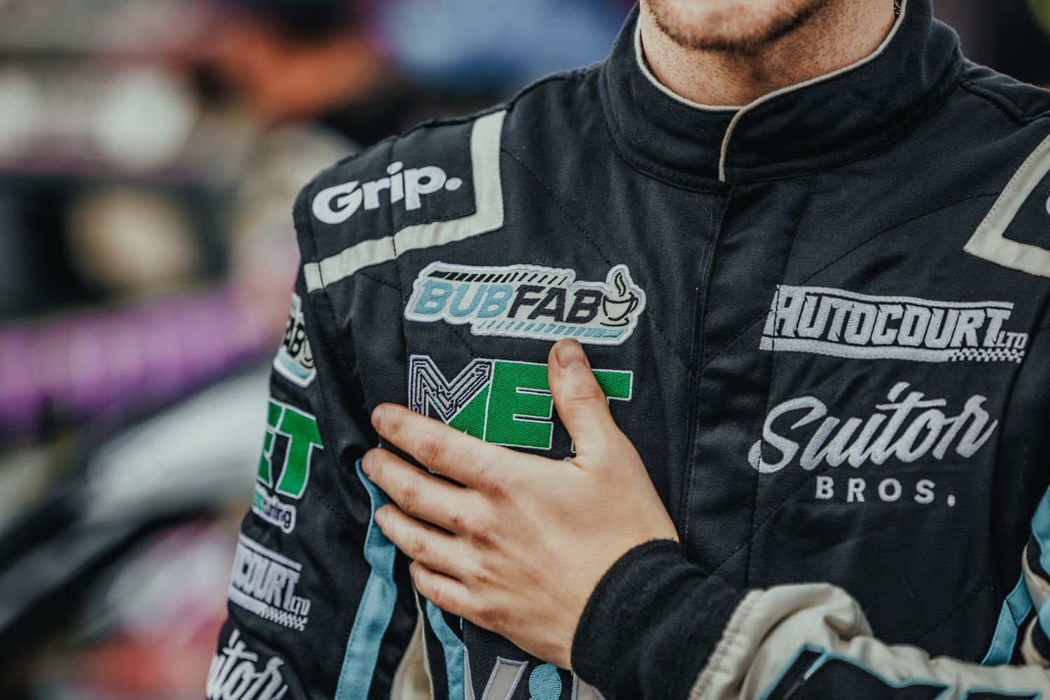 Close-up of racing driver's uniform showing various sponsor logos and patches.