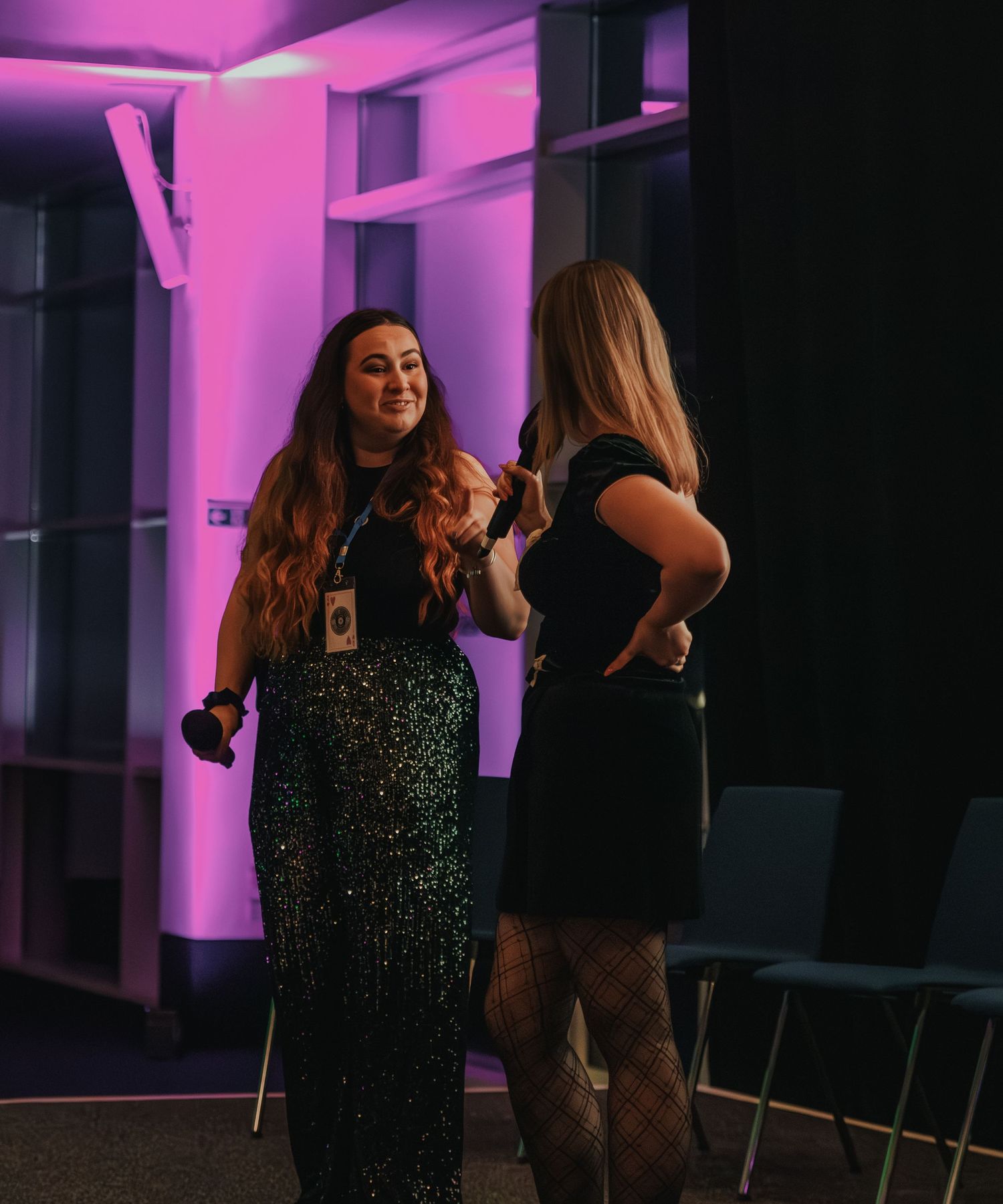 Two people in formal evening wear share a laugh at an event with purple lighting.