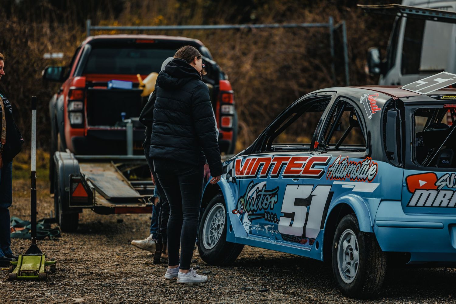 Race car mechanic inspects a light blue race car with number 51 in a pit area.
