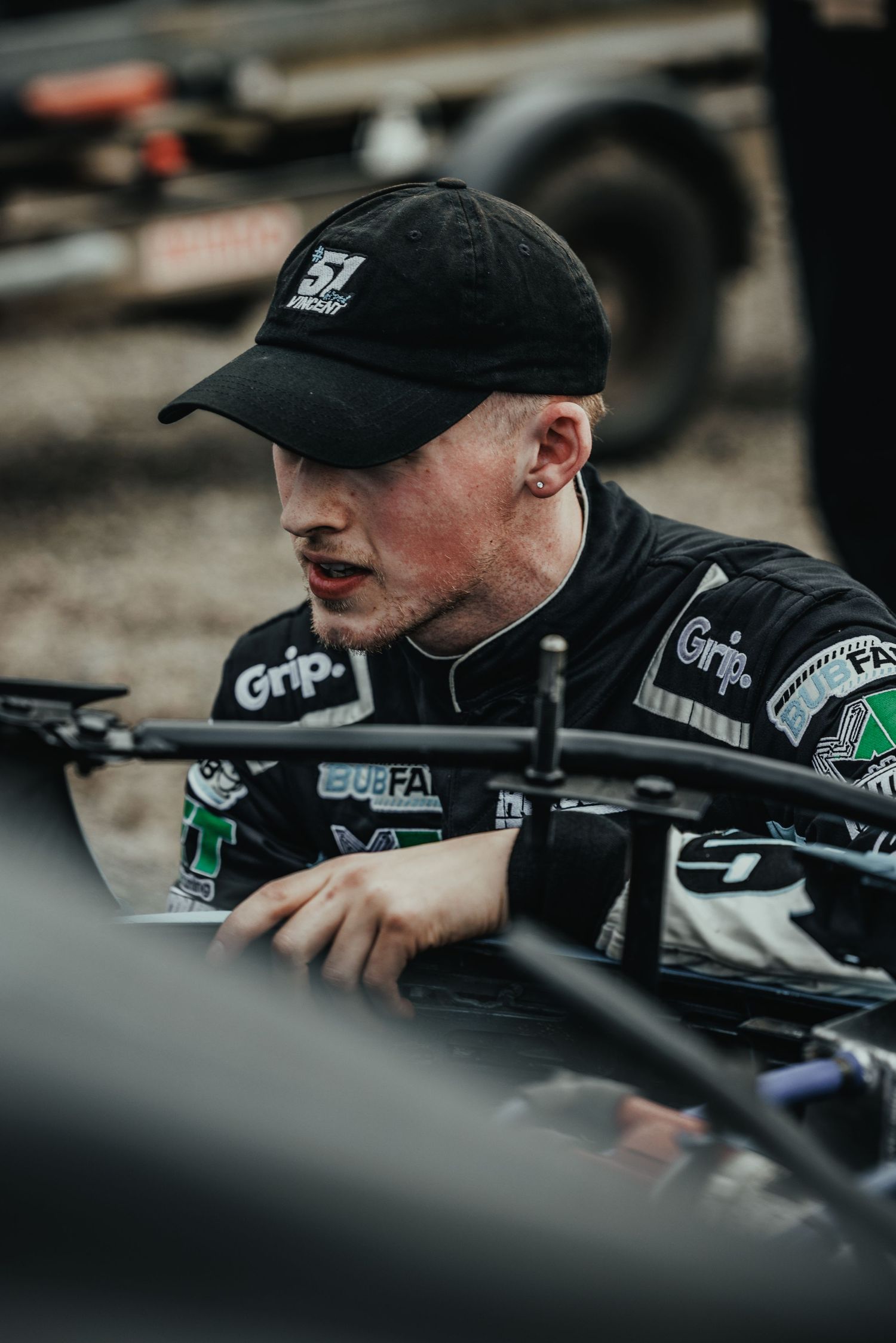 Mechanic in black cap working on race car components during pit stop.