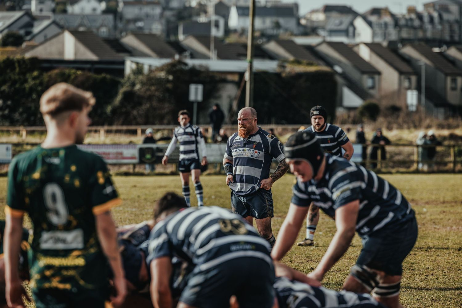 Rugby players line up in striped jerseys for a scrum formation on a sunny field.