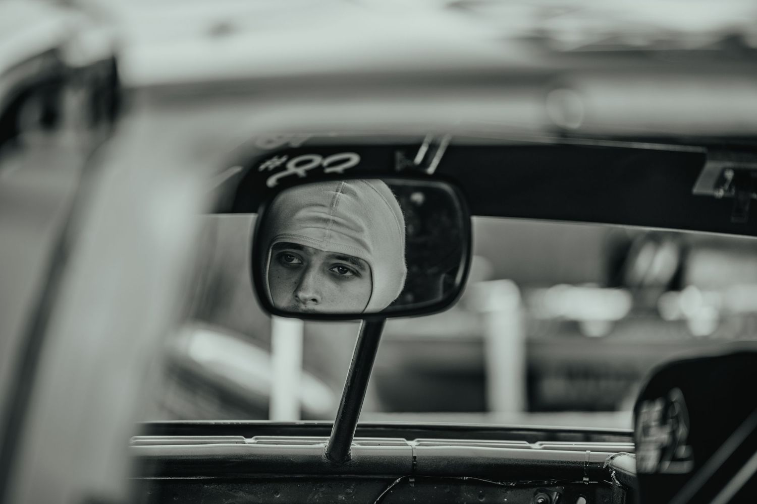 Close up of race car side mirror reflection showing driver with white helmet during motorsport event.