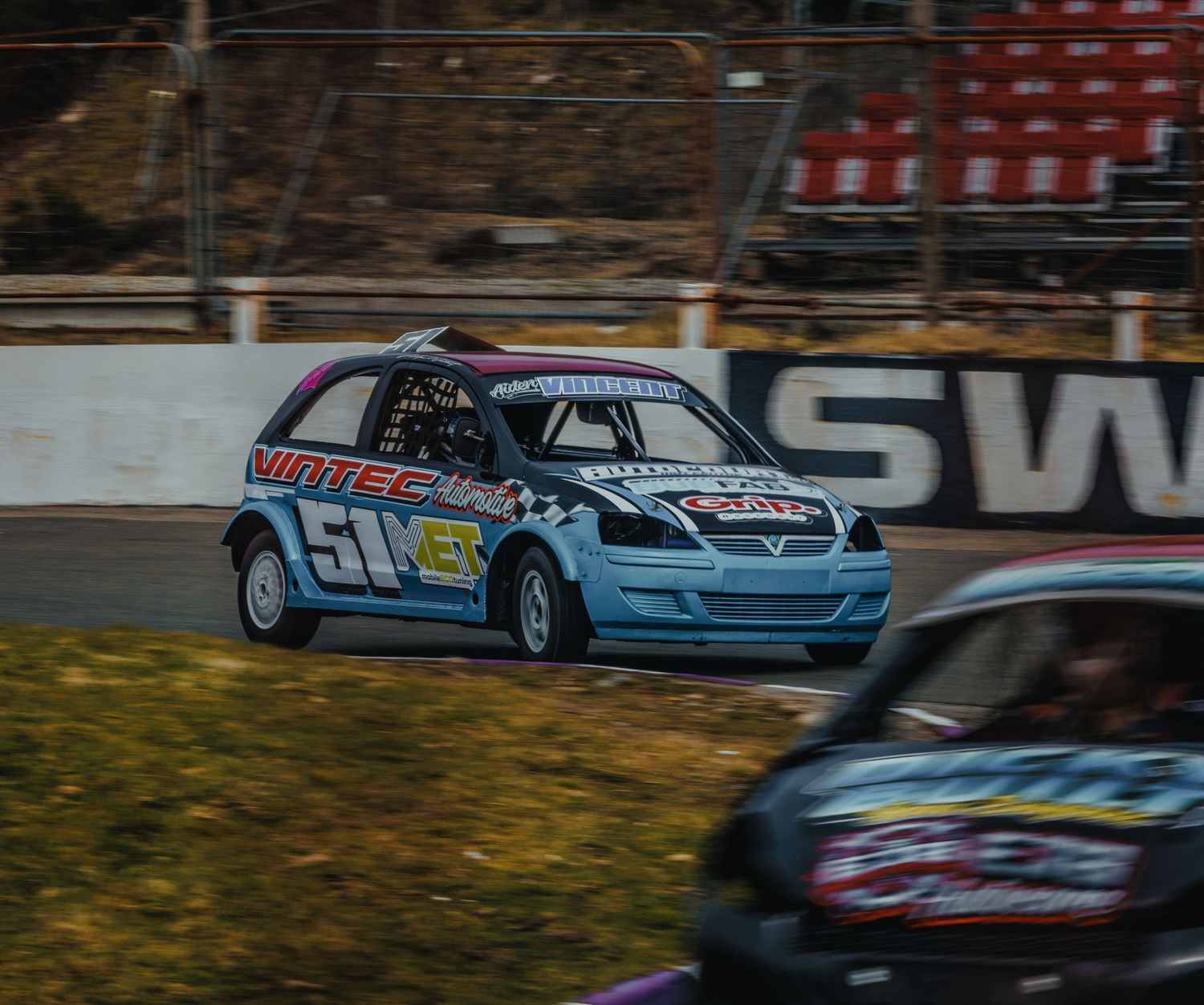 Light blue racing car speeding around track corner during competitive race event.